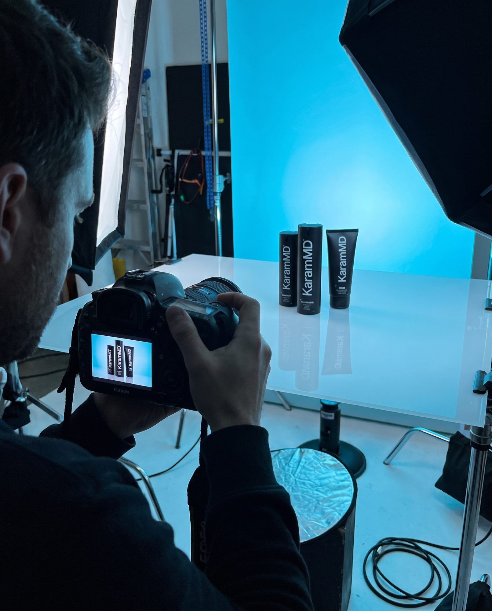 Photographer shooting the KaramMD trio on a lit acrylic sweep against a blue backdrop, the frame visible on the camera's screen