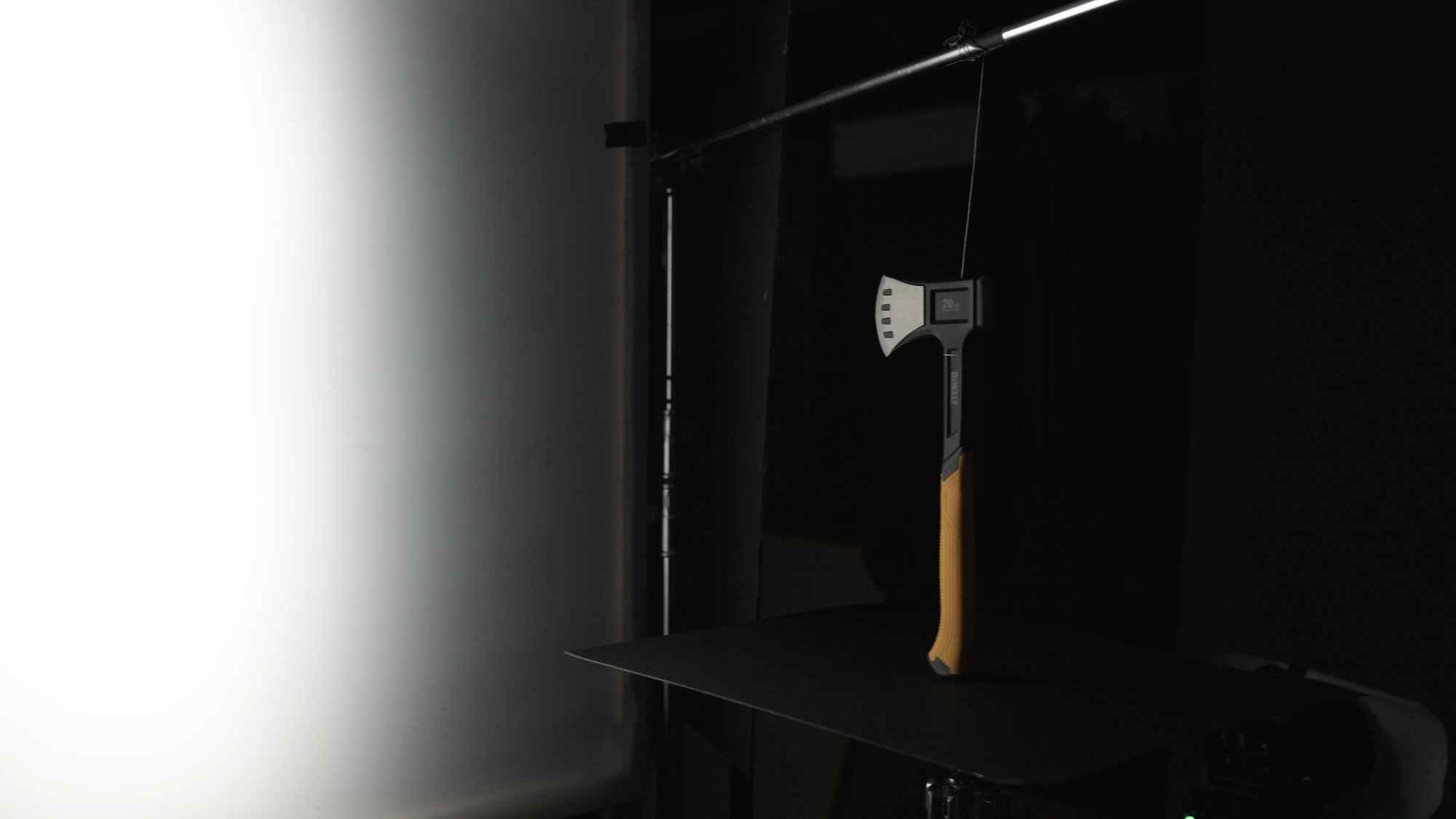 Behind the scenes — DeWalt hatchet suspended on fishing line over a black tabletop, lit by a strip softbox